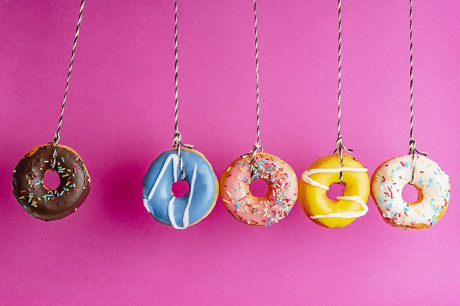 Bunte Donuts hängen, vor einem pinken Hintergrund, in einer Reihe nebeneinander.