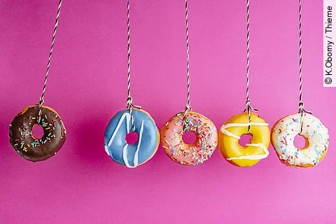 Bunte Donuts hängen, vor einem pinken Hintergrund, in einer Reihe nebeneinander.