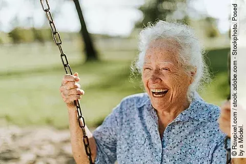 Alte Frau schaukelt lachend in einem Garten