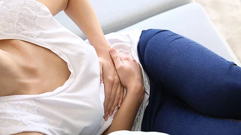 Junge Frau mit Bauchschmerzen liegt auf dem Sofa und hält sich den Bauch.