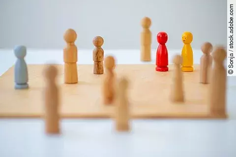 Figuren aus Holz auf einem Holzbrett. Eine rote und gelbe Figur stechen heraus.