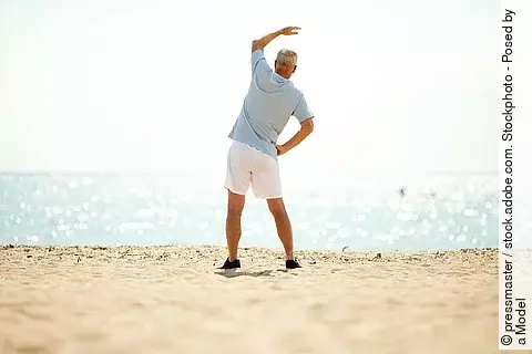Älterer Mann macht Dehnübungen am Strand