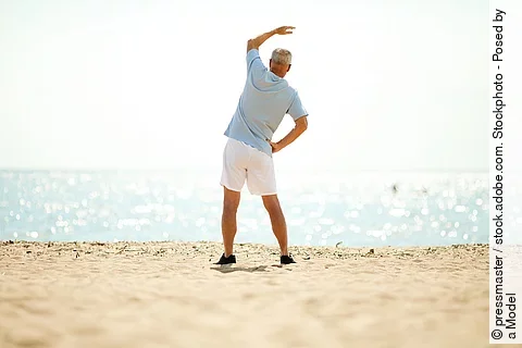 Älterer Mann macht Dehnübungen am Strand