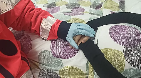 Eine Rettungskraft hält die Hände einer älteren Person am Bett.