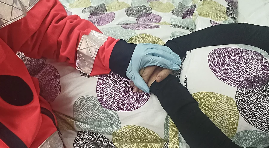 Eine Rettungskraft hält die Hände einer älteren Person am Bett.