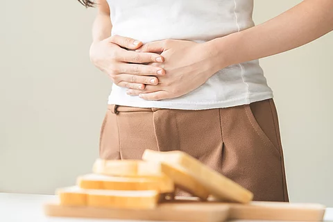 Frau steht vor einem Tisch mit Weißbrotscheiben, hält sich den Bauch