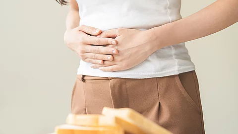 Gluten allergy, asian young woman hand push out, refusing to eat white bread slice on chopping board in food meal at home, girl having a stomach ache. Gluten intolerant and Gluten free diet concept. Frau steht vor einem Tisch mit Weißbrotscheiben, hält sich den Bauch