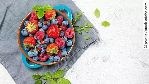 verschiedene frische Beeren in einem Topf auf grauem Leinentuch 