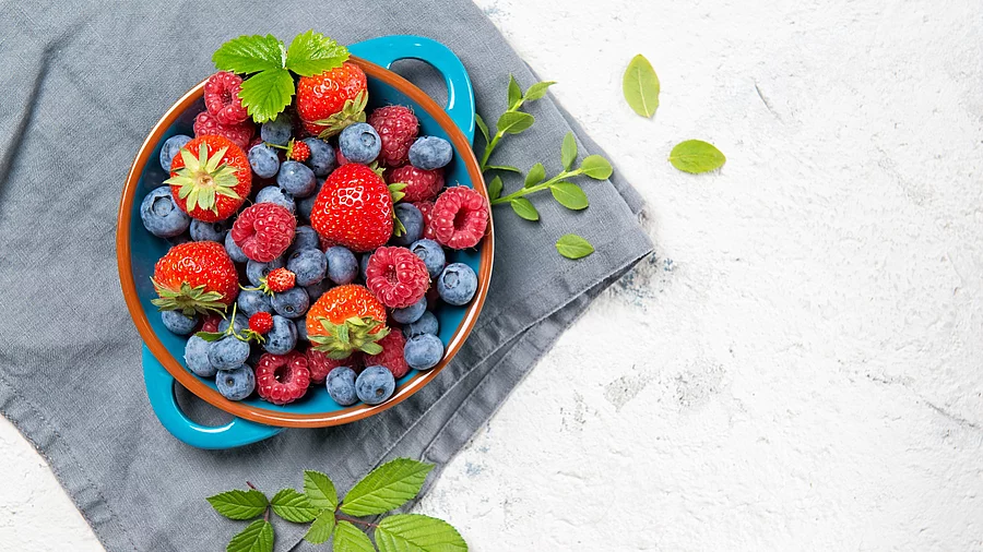 verschiedene frische Beeren in einem Topf auf grauem Leinentuch 