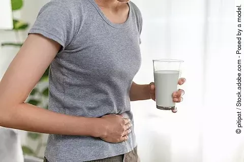 Frau mit einem Glas Milch in der Hand hält sich den Bauch.