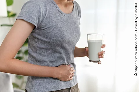 Frau mit einem Glas Milch in der Hand hält sich den Bauch.
