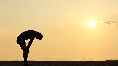 Silhouette of an exhausted sportsman at sunset Silhouette eines gebeugt stehenden, erschöpften Sportlers vor Sonnenuntergang