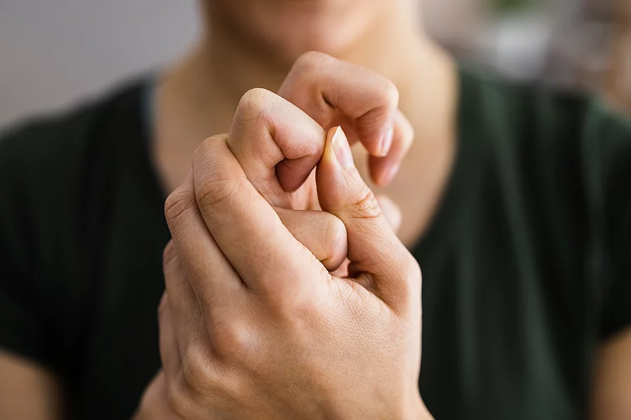 Frau mit rheumatisch gekrümmten Fingergelenken hält sich die Hände