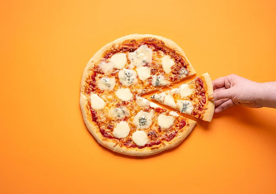 Hand greift nach einem Stück aus einer Pizza Hand greift nach einem Stück aus einer Pizza