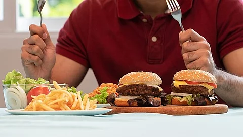 Mann mit Messer und Gabel am Tisch mit Burger, Pommes und Salat