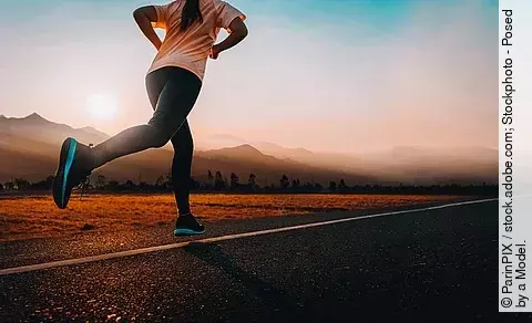 Frau joggt auf einer Straße dem Sonnenuntergang entgegen