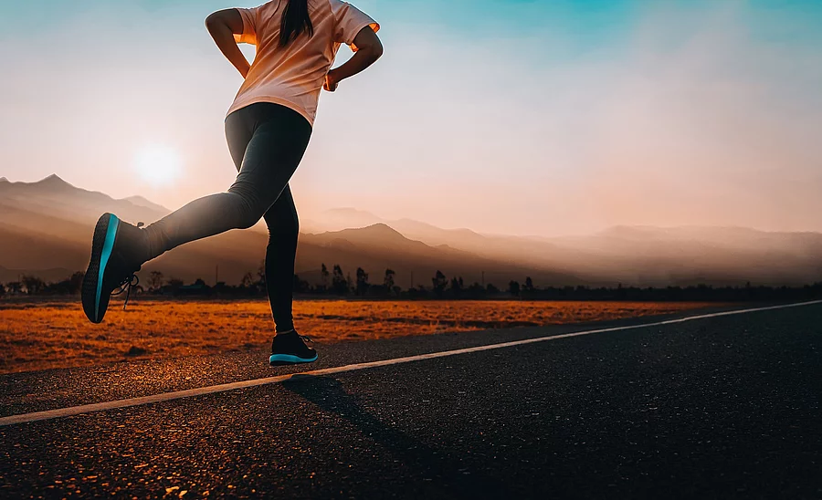Frau joggt auf einer Straße dem Sonnenuntergang entgegen