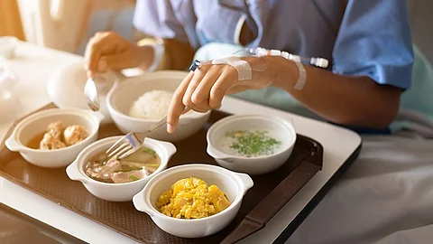 Patient liegt im Krankenbett mit einem Tablett voller Essen vor sich. 