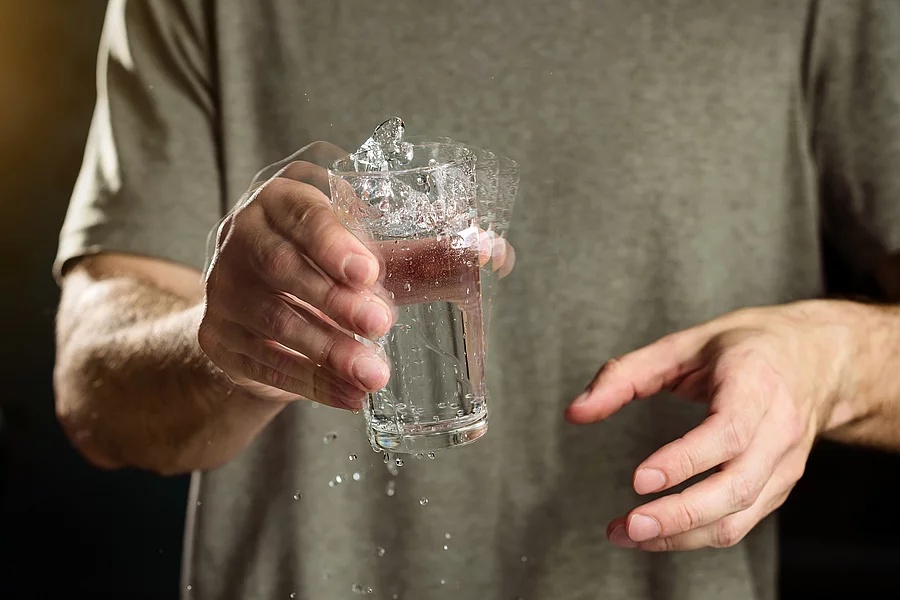 A man holds a glass of water with a shaking hand. The concept of parkinson's disease and tremor. Mann hält Wasserglas mit zitternder Hand