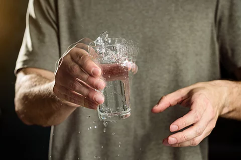 Mann hält Wasserglas mit zitternder Hand