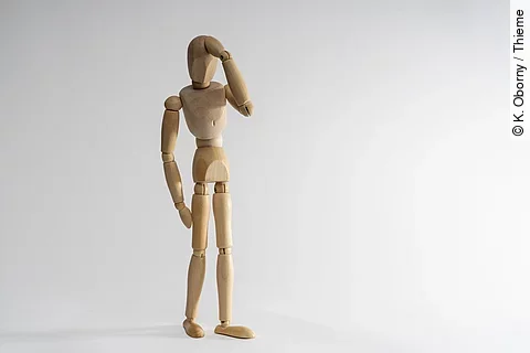 Holzpuppe hält sich die Hand an den Kopf.
