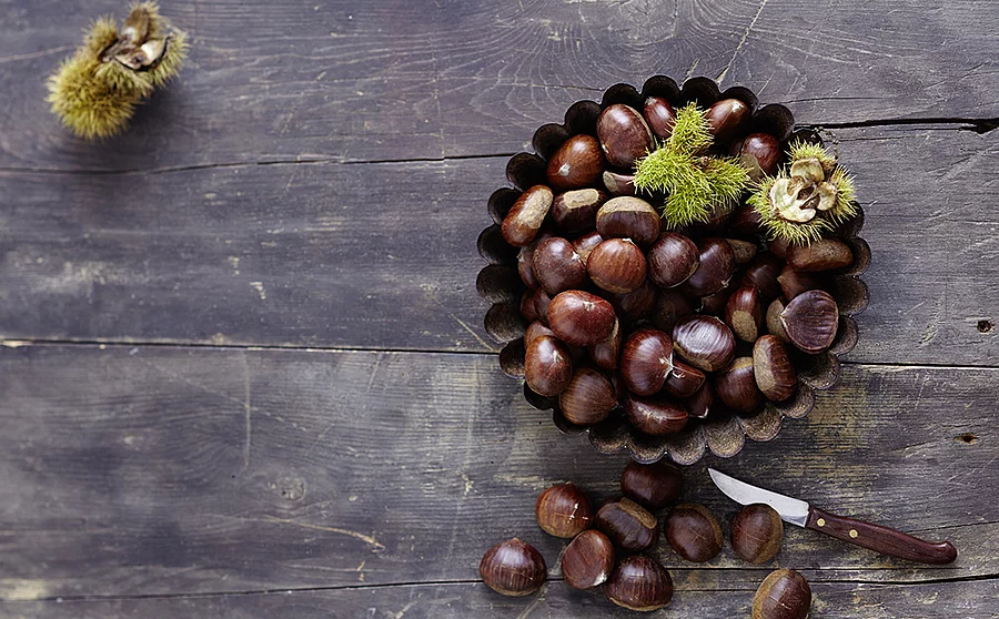 Esskastanien in einer Schale auf einem Holztisch, daneben ein Messer