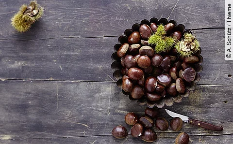 Esskastanien in einer Schale auf einem Holztisch, daneben ein Messer