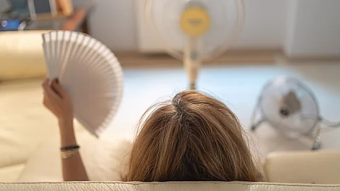 Rückansicht einer Frau auf Sofa mit Ventilatoren und Fächer