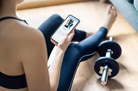 Frau sitzt auf einer Yoga-Matte und macht mit einer App Sport.