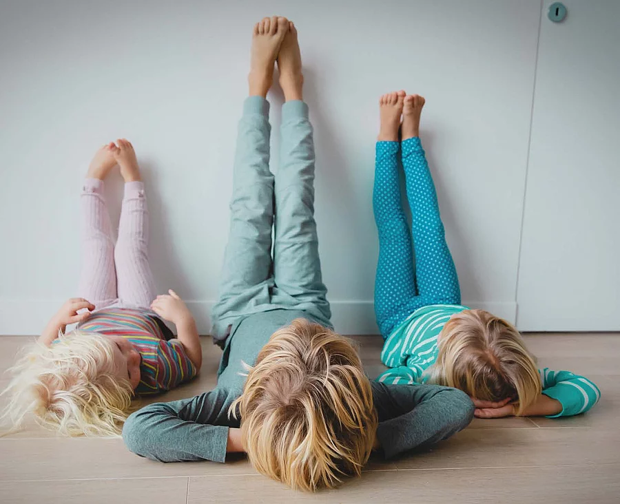 drei Kinder liegen auf dem Boden und strecken die Beine nach oben.