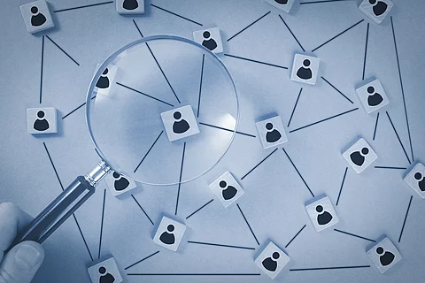 In einer schematischen Darstellungen sind Personen über ein Netzwerk verbunden. Eine Lupe vergrößert einen Ausschnitt des Netzwerks. 