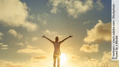 Frau steht bei Sonnenuntergang auf einem Feld und breitet die Arme aus.