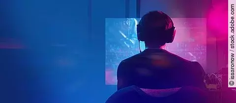 Mann trägt Kopfhörer und sitzt in einem dunklen Zimmer vor seinem PC.