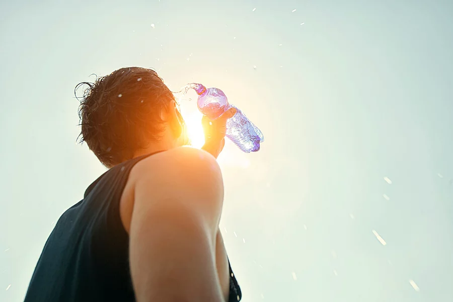 Man übergießt sich mit Wasser aus einer Flasche.
