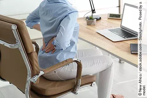 Frau am Schreibtisch dehnt sich den Rücken