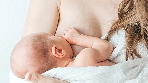 Frau, die ihr Baby auf dem Arm hält und stillt.