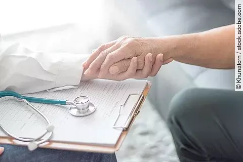 Arzt mit Klemmbrett hält Hand eines älteren Patienten. 