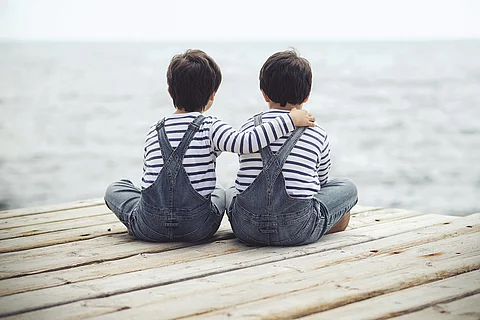 Zwei kleine Kinder sitzen auf Steg und halten sich in den Armen