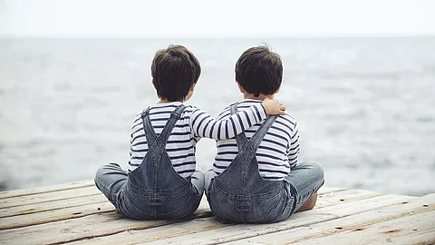Zwei kleine Kinder sitzen auf Steg und halten sich in den Armen