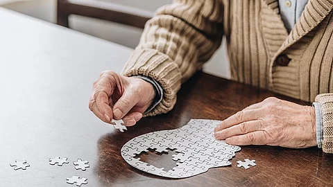 Ein älterer Mann sitzt an einem Puzzle in Form eines Kopfes. 