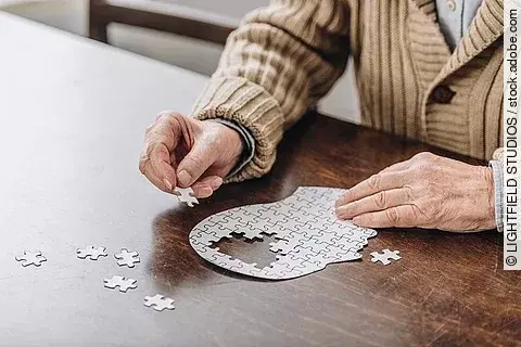 Ein älterer Mann sitzt an einem Puzzle in Form eines Kopfes. 