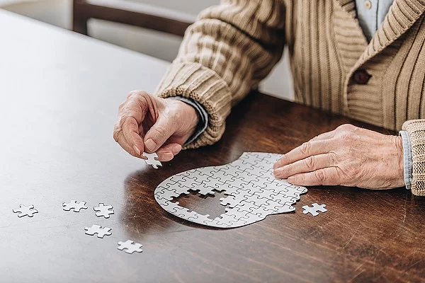 Ein älterer Mann sitzt an einem Puzzle in Form eines Kopfes. 