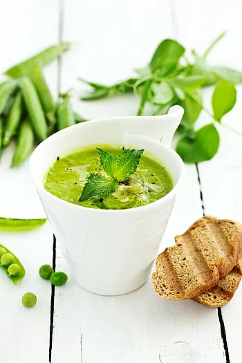 Erbsensuppe in einer weißen Tasse mit Minzblatt