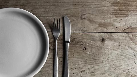 leerer Teller und Besteck auf Holztisch, Symbolbild Fasten