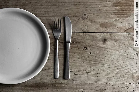 leerer Teller und Besteck auf Holztisch, Symbolbild Fasten