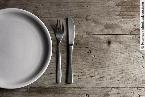 leerer Teller und Besteck auf Holztisch, Symbolbild Fasten