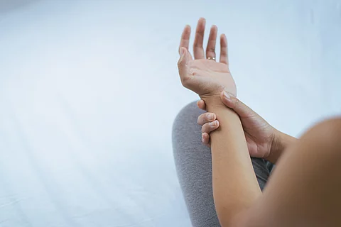 Frau hält ihren schmerzenden Arm fest. 