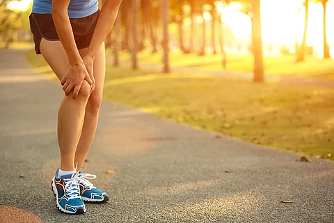Frau in Sporthose beim Joggen, hält sich ihr schmerzendes Knie