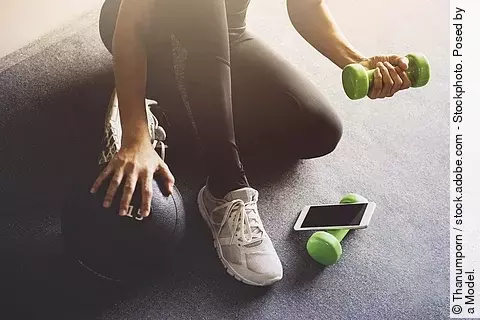 Frau in Sportkleidung mit Hanteln und Smartphone
