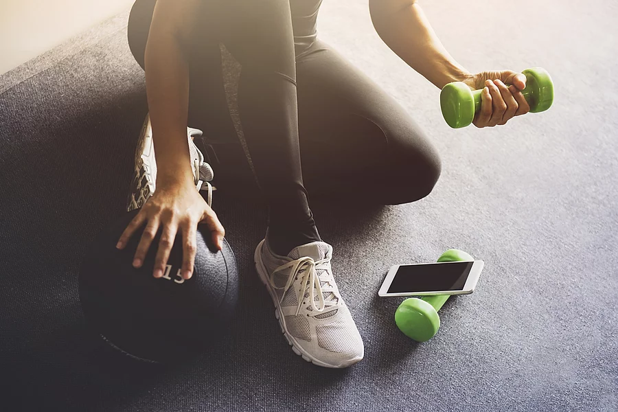 Frau in Sportkleidung mit Hanteln und Smartphone